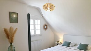 Ein Schlafzimmer mit einem großen Bett, einem Nachttisch mit Lampe, einem Heizkörper, einem Fenster mit Vorhängen und einer Wandleuchte.