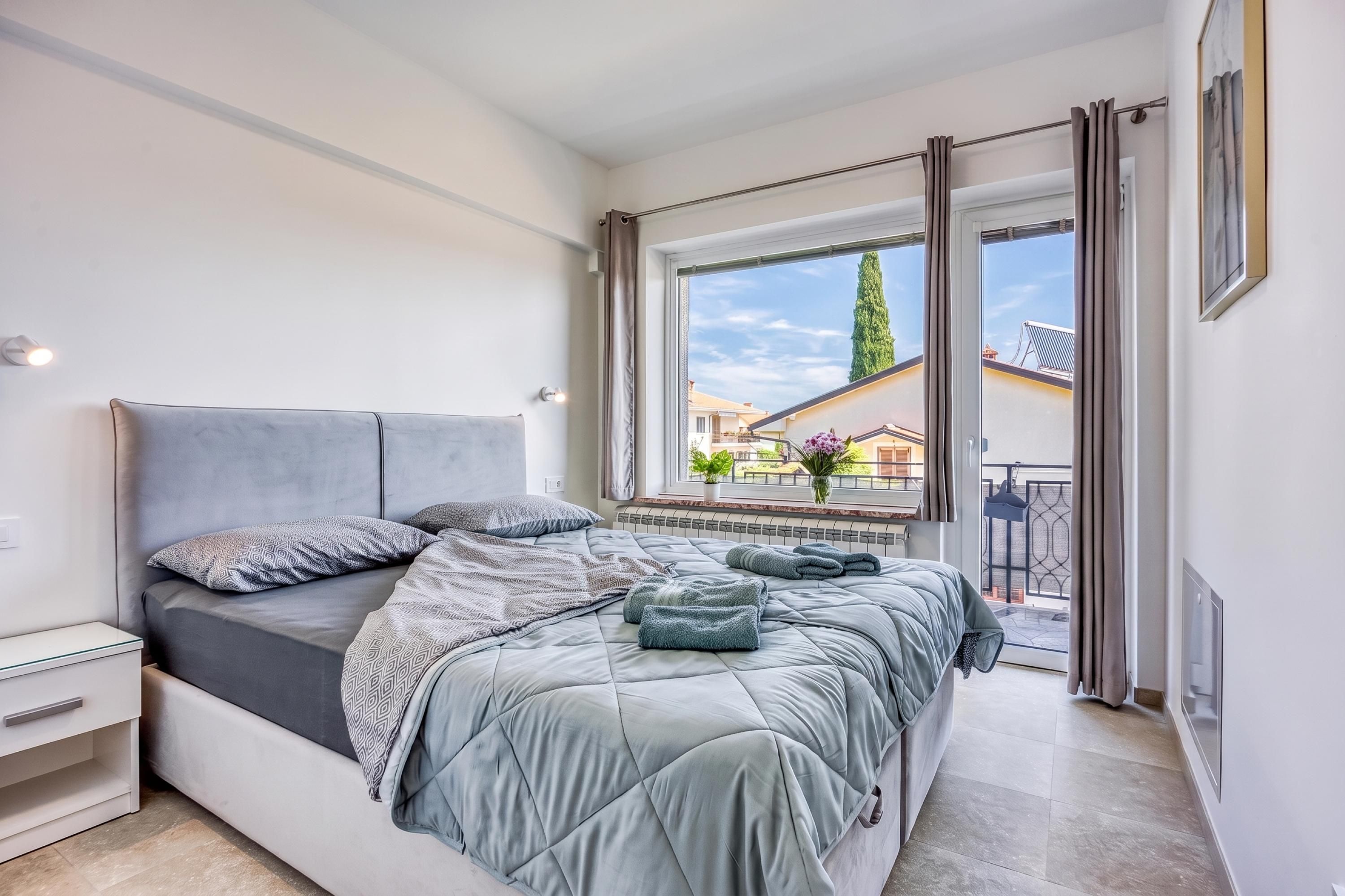 A bedroom with a bed, bedside table, and a window with a view of the outside.