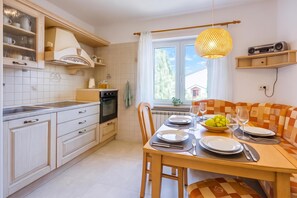Uma cozinha moderna com área de jantar, apresentando uma mesa de madeira posta para dois, forno embutido e janela com vista.