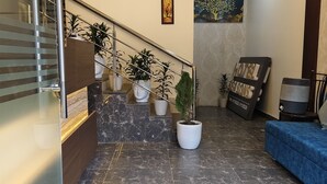 Un hall d’hôtel moderne avec un escalier en marbre, des plantes en pot et un canapé bleu.