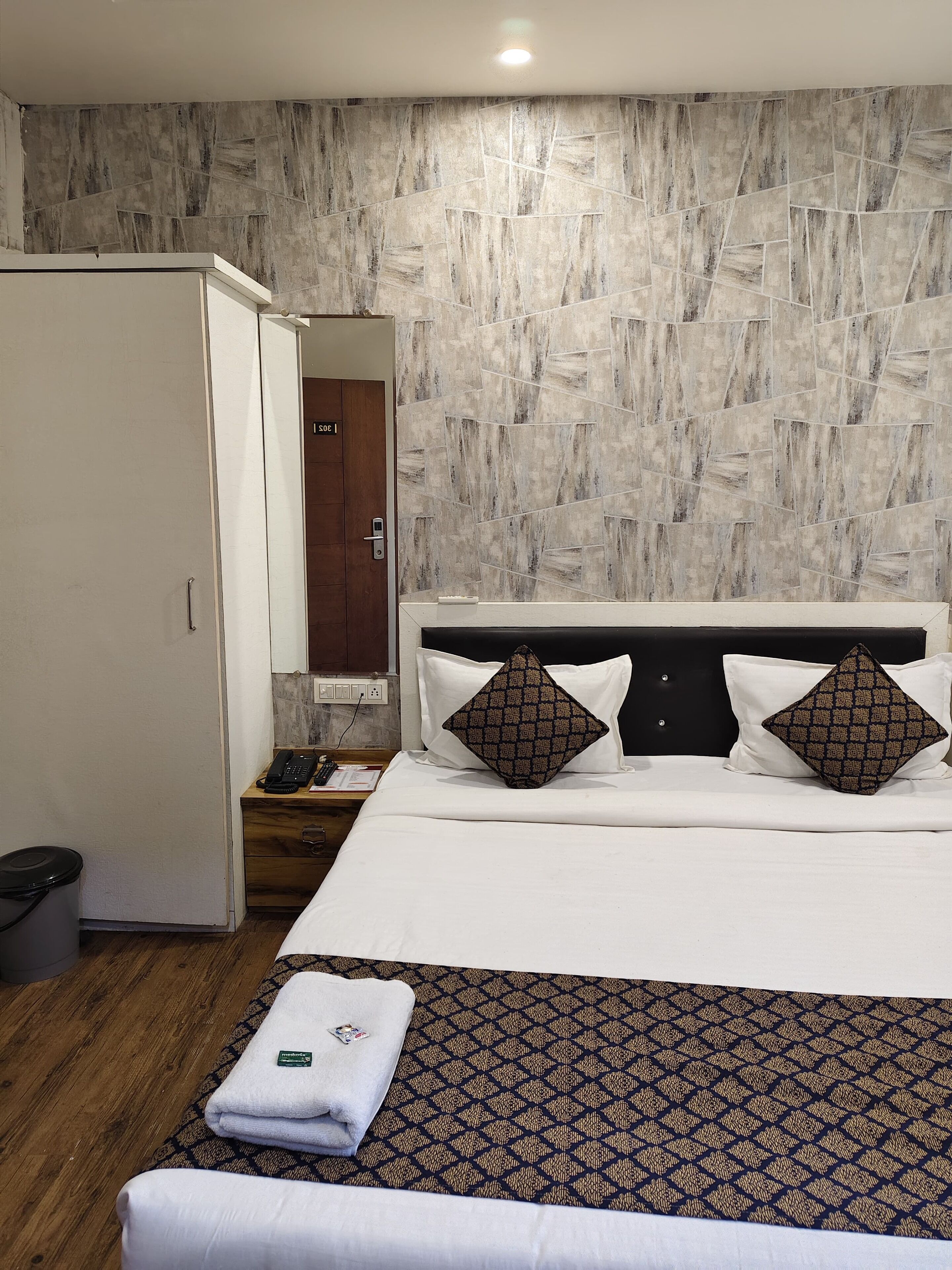Een hotelkamer met een bed, een kledingkast, een nachtkastje met een telefoon en een kamerkleed met dessin.
