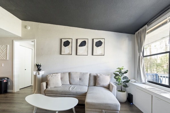Un salon avec un canapé, une petite table, une plante en pot et trois œuvres d’art encadrées accrochées au mur.