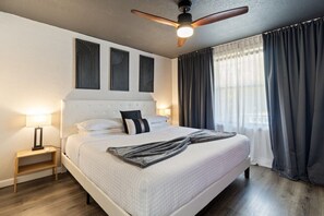 Ein Hotelzimmer mit einem Bett, einem Nachttisch, einem Deckenventilator und einem Fenster mit Vorhängen.