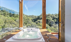 Un jacuzzi en una terraza de madera con vista a una ladera boscosa.