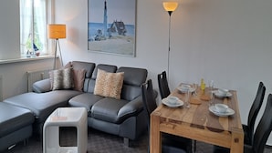 Una sala de estar moderna con un sofá, una mesa de comedor dispuesta para dos personas y un cuadro de un faro.
