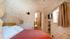 A room with a bed, a television, and a stone wall. - Villa 'Dimora Dormio' with Private Pool, Wi-Fi, and Air Conditioning (monopoli)