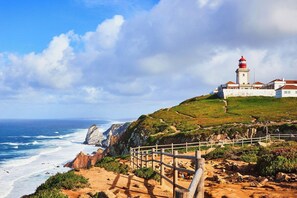 Paesaggio costiero con un faro, terreno roccioso e una vista limpida sull'oceano.