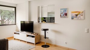 A modern living room with a flat-screen TV, a white entertainment unit, a black bar stool, and two framed artworks on the wall. - The Light Stay at Cascais (Cascais)