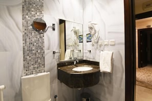 Casa de banho com lavatório de mármore, um espelho grande, um porta-toalhas e uma sanita.
