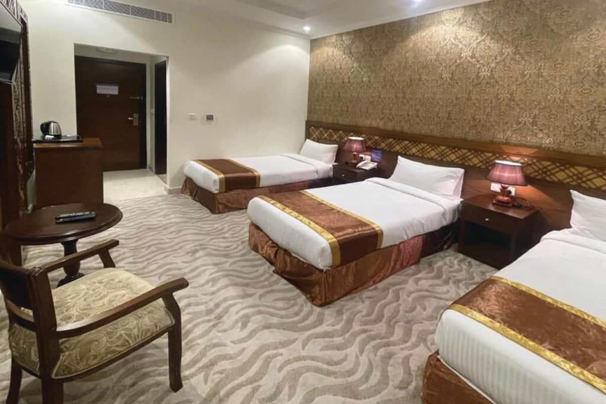 A hotel room with three beds, a wooden desk, a chair, and a patterned carpet.