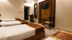 A hotel room with three beds, a television, a desk, and a chair. - Retaj Inn Hotel (Makkah)