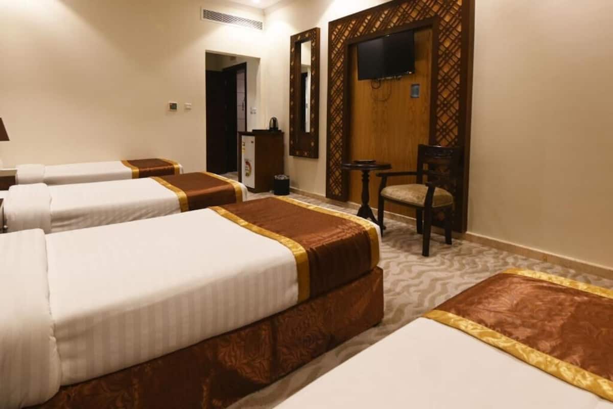 A hotel room with three beds, a television, a desk, and a chair.