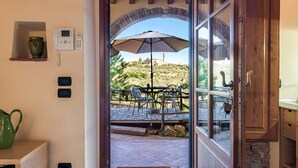 An open door leading to an outdoor patio with a table and chairs, a large umbrella, and a view of a hill with a building in the distance. - Studio 'Libeccio' with Shared Pool, Wi-Fi and Air Conditioning (Scandicci)