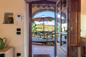 An open door leading to an outdoor patio with a table and chairs, a large umbrella, and a view of a hill with a building in the distance. - Studio 'Libeccio' with Shared Pool, Wi-Fi and Air Conditioning (Scandicci)