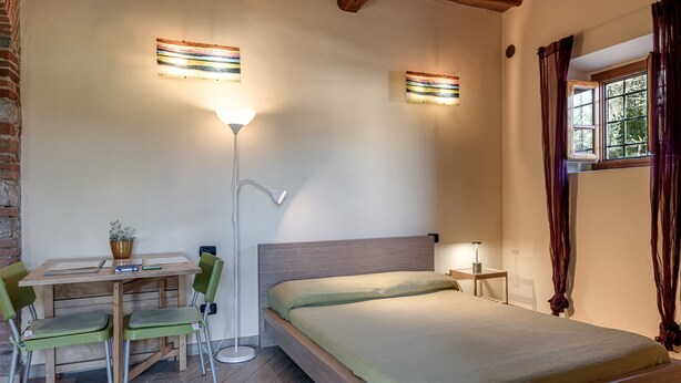 A bedroom with a bed, a desk with chairs, a floor lamp, and a window with curtains. - Studio 'Libeccio' with Shared Pool, Wi-Fi and Air Conditioning (Scandicci)