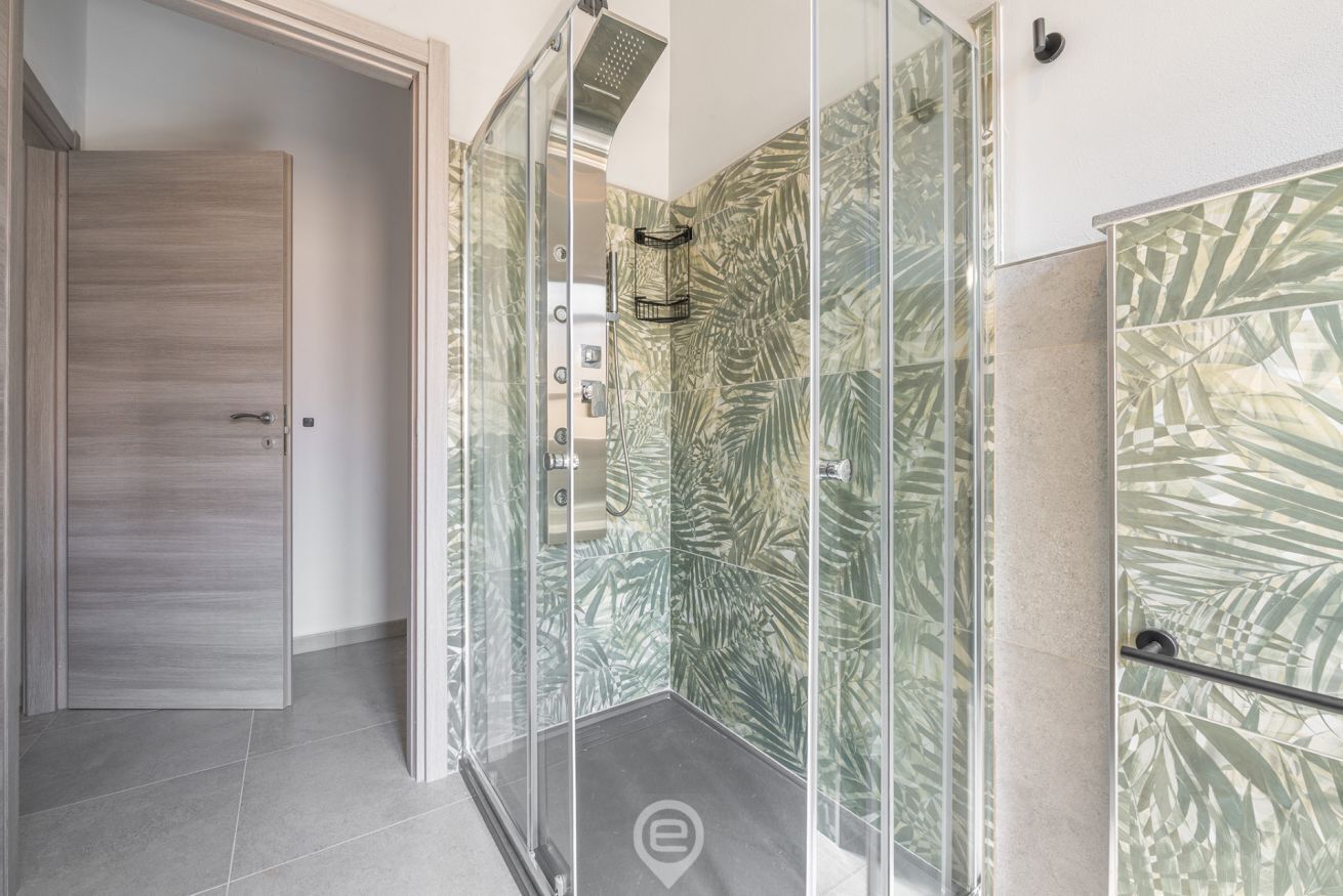A modern bathroom with a glass shower enclosure, a wooden door, and patterned tiles.