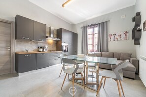 Una cocina moderna con armarios oscuros, una mesa de comedor de vidrio y un sofá gris en la sala de estar.