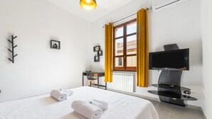 A hotel room with a bed, a desk, a chair, a TV, and a window with curtains. - Cagliari Shopping District Flat (Cagliari)