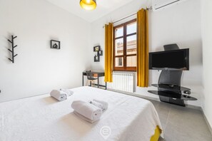 A hotel room with a bed, a desk, a chair, a TV, and a window with curtains. - Cagliari Shopping District Flat (Cagliari)