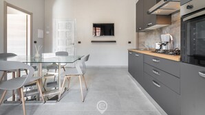 A modern kitchen with a glass dining table, grey chairs, and a built-in stove. - Cagliari Shopping District Flat (Cagliari)