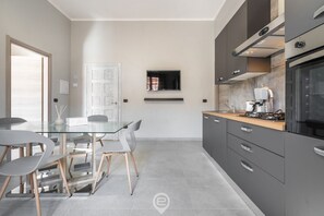 A modern kitchen with a glass dining table, grey chairs, and a built-in stove. - Cagliari Shopping District Flat (Cagliari)