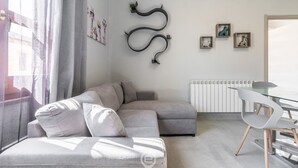 Un salon moderne avec un canapé d’angle gris, une table à manger en verre accompagnée d’une chaise, et un élément décoratif fixé au mur.