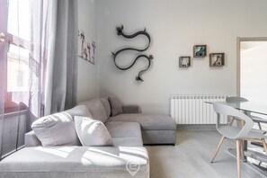 Una sala de estar moderna con un sofá seccional gris, una mesa de comedor de vidrio con una silla y un adorno colgado en la pared.