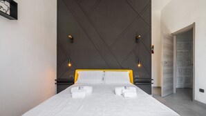 Une chambre d’hôtel moderne avec un grand lit, un panneau mural géométrique de couleur sombre et une porte située à droite.