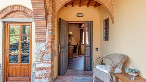 Una scala in pietra conduce a una porta di legno, una sedia in vimini e un tavolino con una pianta.