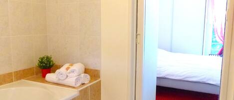 A bathroom with a bathtub, a small potted plant, and rolled towels on a shelf.