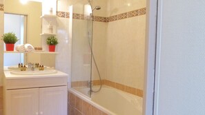 A bathroom with a glass-enclosed shower, a sink with toiletries, and a mirror. - Cosy flat close to the centre of Auray (Auray)