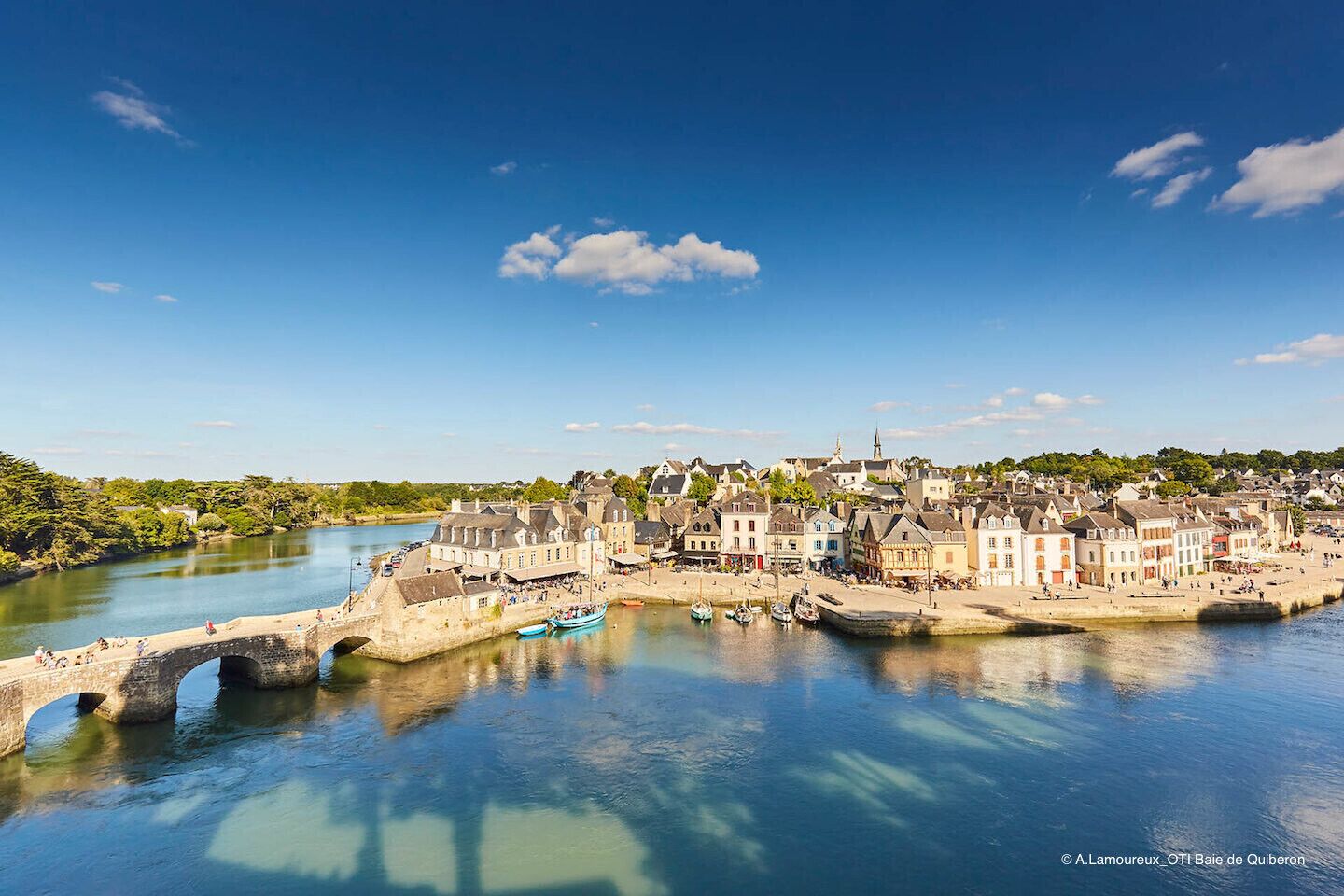 Un pueblo histórico con un río, un puente de piedra y barcos.