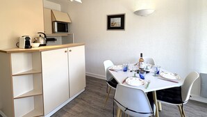 A compact kitchen with a microwave, kettle, and toaster, a dining table set for four, and a framed picture on the wall. - Jetée des Marins by Interhome (Arcachon)