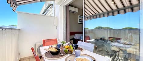 A balcony with a table set for breakfast, including toast, fruit, and a coffee cup.