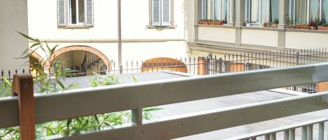 A balcony with a wooden table and a red chair, overlooking a building with multiple windows and a tiled roof.