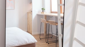 Une petite pièce comprenant un lit, un bureau avec deux chaises, une fenêtre et une porte.