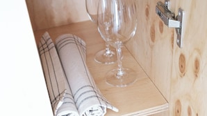 Un meuble en bois à deux étagères ; l’étagère supérieure contient des serviettes enroulées et un verre à vin, et l’étagère inférieure abrite une assiette, des couverts et deux verres.