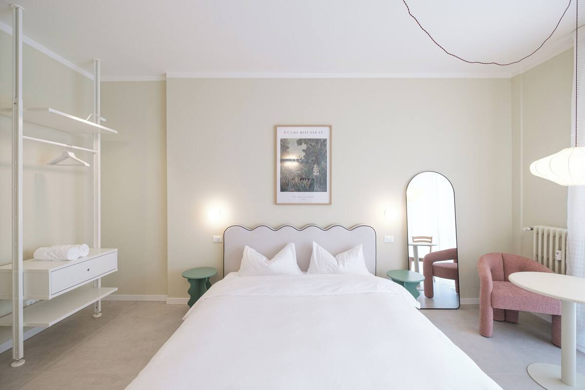 A neatly arranged bedroom with a bed, a wardrobe, a chair, a table, and a mirror.
