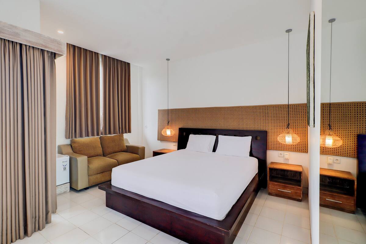Een moderne hotelkamer met een groot bed, een slaapbank, een houten hoofdbord en twee nachtkastjes met lampen.