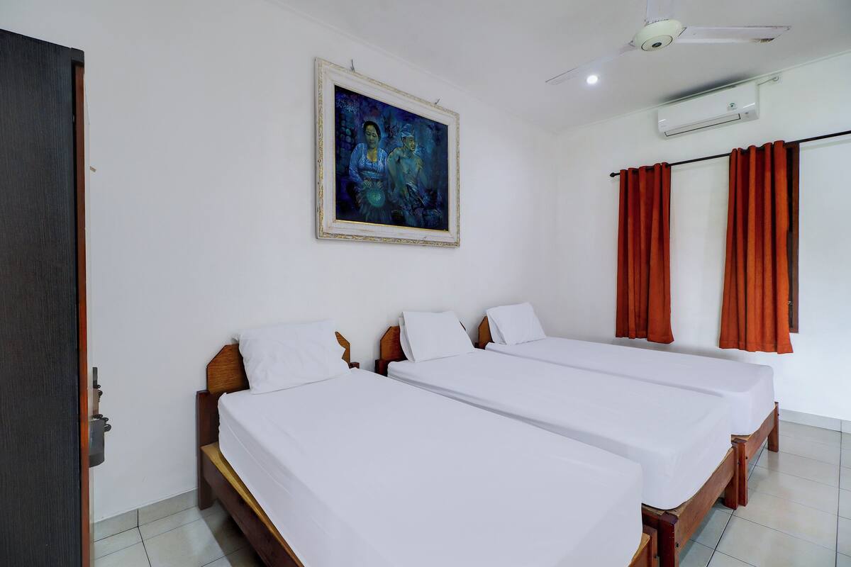 Een hotelkamer met twee enkele bedden, een plafondventilator, een airconditioning en een schilderij aan de muur.
