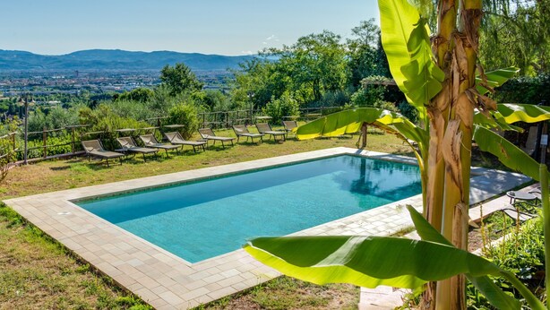 A rectangular swimming pool with a tiled border, surrounded by lounge chairs and a view of distant mountains.