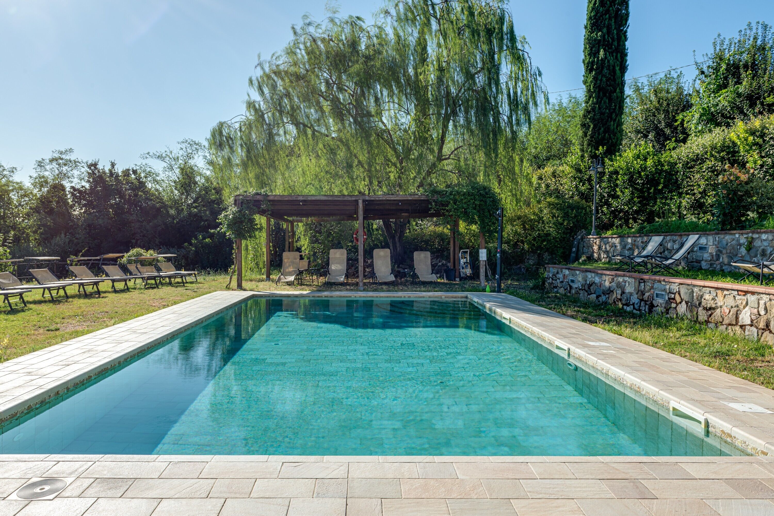 A rectangular swimming pool with a pergola and lounge chairs in a landscaped garden.