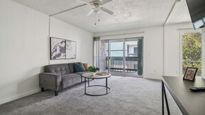 Un salon avec un canapé gris, une table basse ronde, un ventilateur de plafond et un balcon avec vue.