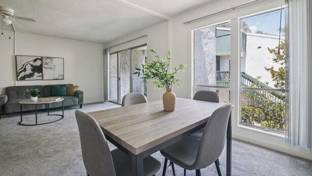 Un salon moderne avec une table à manger, un canapé gris et une grande fenêtre donnant sur l’extérieur.