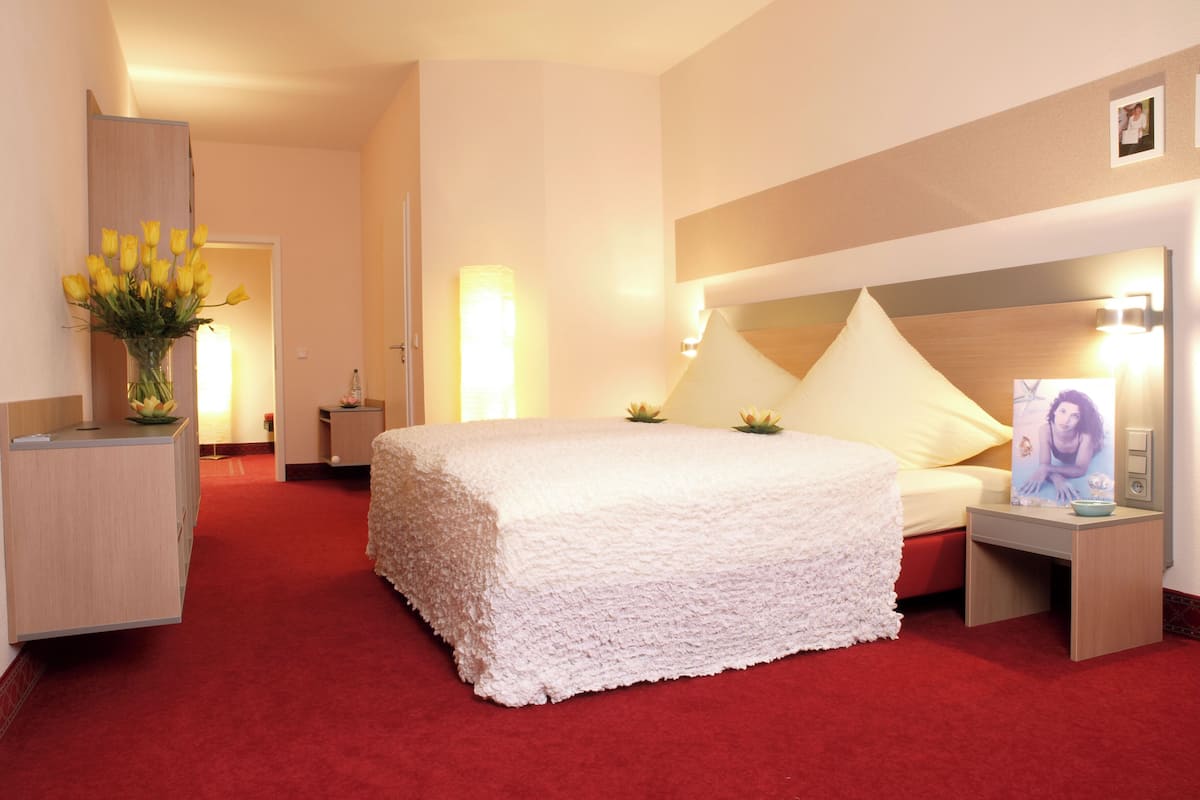 A hotel room with a large bed, a bedside table, a nightstand, a vase with flowers, and a picture on the wall.