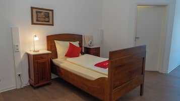 A wooden bed with a headboard, a bedside table with a lamp, a nightstand, and a framed picture on the wall.
