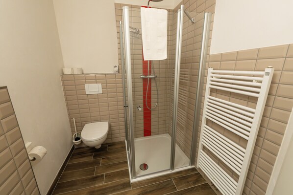 A modern bathroom with a glass shower enclosure, a white toilet, and a towel rack.