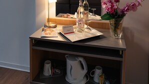 Une chambre d’hôtel équipée d’un bureau, d’un miroir, d’un lit, d’une table de chevet, d’un vase avec des fleurs, d’une lampe et d’une machine à café.