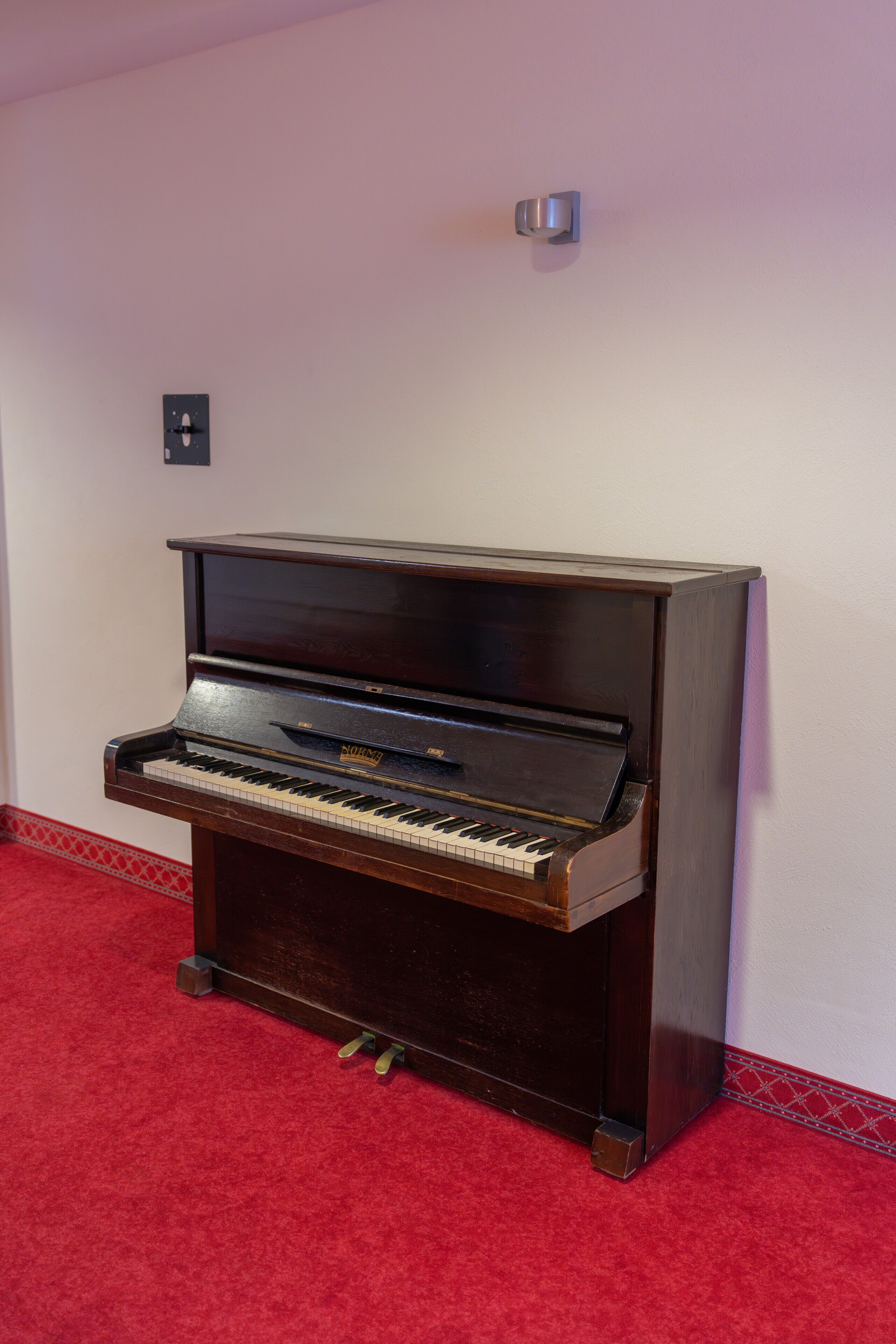 Un piano de cola en una habitación con alfombra roja y pared blanca.