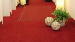 Un couloir d'hôtel avec un tapis rouge, de nombreuses portes et des lampes fixées au mur.